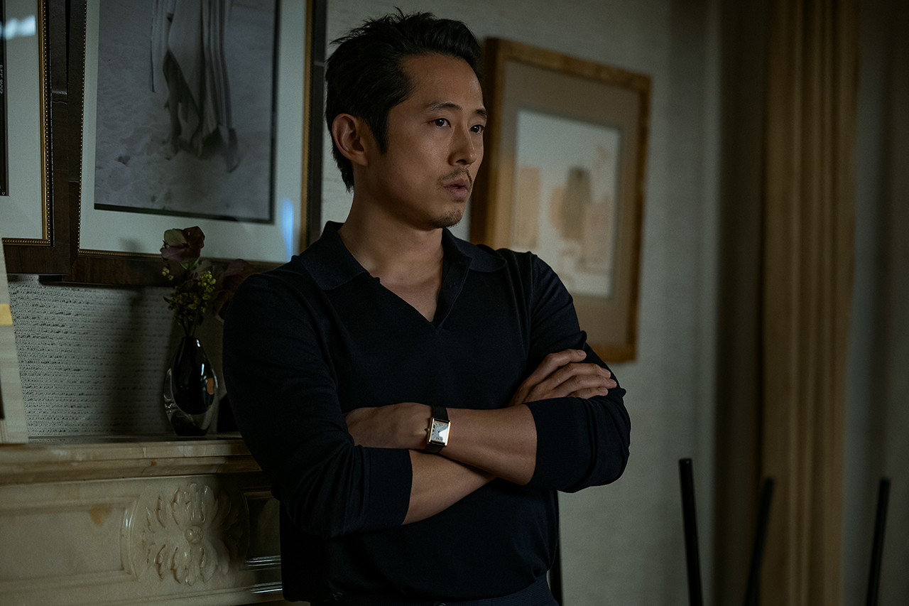 &Quot;Man In Dark Clothing Stands Indoors With Arms Crossed, Leaning Against A Mantel With Framed Pictures And A Vase, In A Softly Lit Room With Neutral Decor And Curtains In The Background.&Quot;