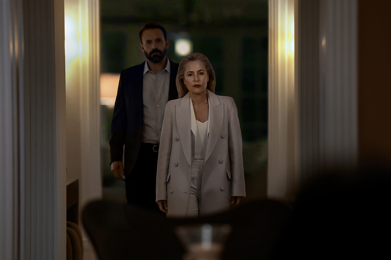 &Quot;A Woman In A Light Suit And A Man In A Dark Suit Stand In A Dimly Lit Hallway, Framed By White Columns, Facing The Camera With Serious Expressions, Suggesting A Tense Or Formal Setting.&Quot;