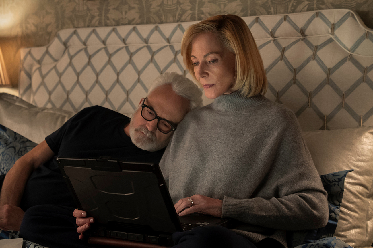 &Quot;Older Couple Relaxing In Bed Together, Man Resting His Head On Woman's Shoulder While She Uses A Tablet, Cozy Bedroom Setting With Patterned Headboard And Soft Lighting.&Quot;