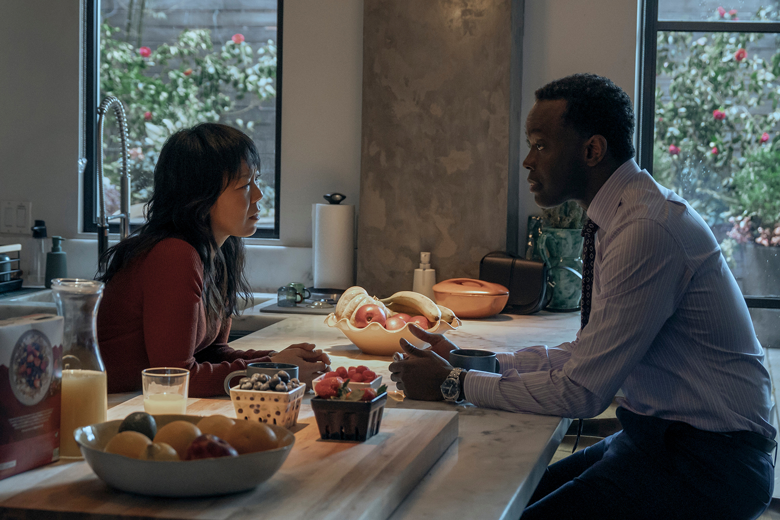 &Quot;Two People Sitting At A Kitchen Island Having A Serious Conversation, Surrounded By Fruit, Juice, And Soft Daylight From Large Windows With A View Of A Garden Outside.&Quot;