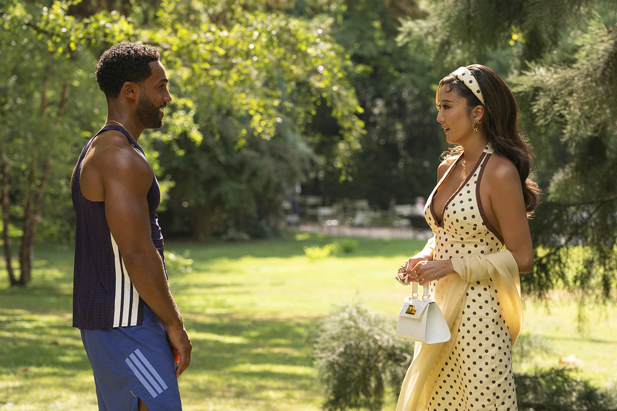 &Quot;A Man In Athletic Wear And A Woman In A Yellow Polka Dot Dress Stand Facing Each Other In A Sunlit Park Surrounded By Trees, Engaged In Conversation On A Summer Day.&Quot;