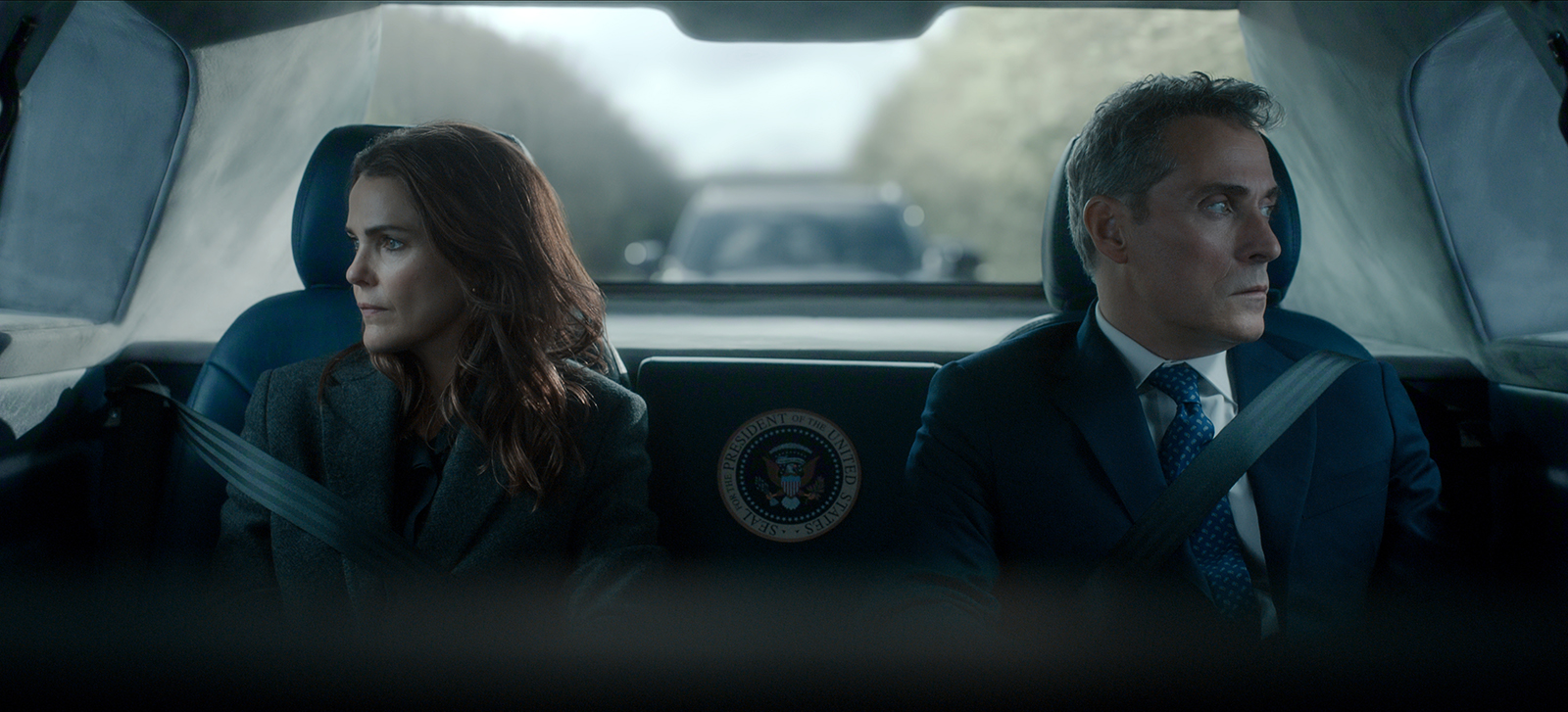 &Quot;Two Serious People In Formal Attire Sit In The Back Of A Car With A Presidential Seal, Looking Out The Windows; The Environment Is Tense, With Another Vehicle Visible Behind Them Through The Rear Window.&Quot;