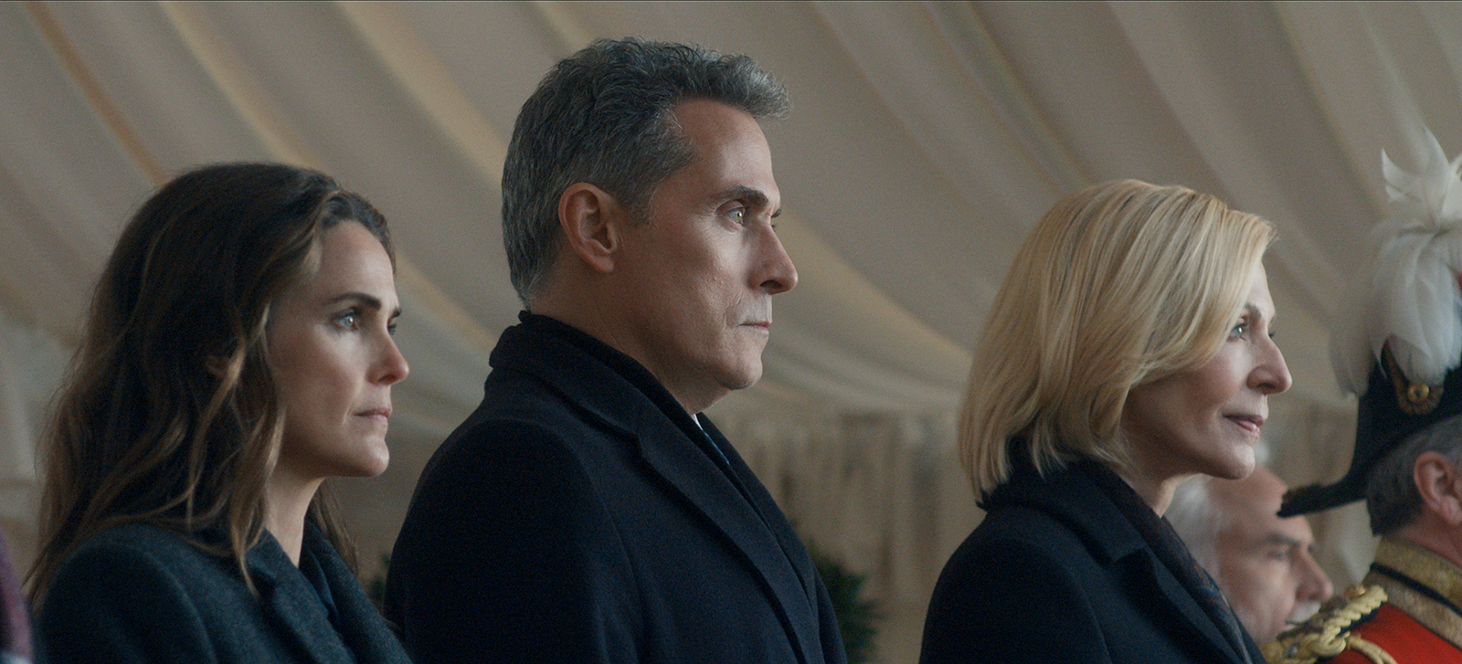 &Quot;Three Serious-Looking Adults In Formal Dark Clothing Stand Side By Side In An Elegant, Tented Environment. They Are Watching Something Intently, Possibly At An Official Event Or Ceremony. A Uniformed Figure Is Partially Visible.&Quot;