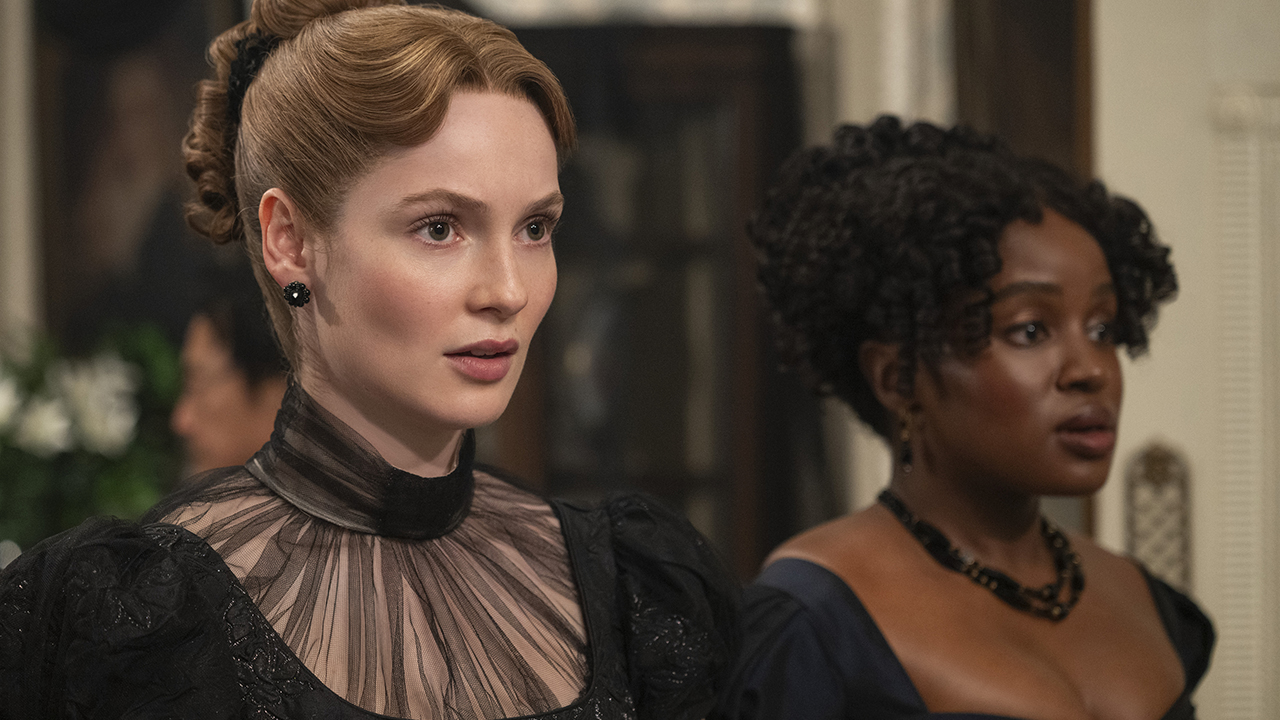 &Quot;Two Women Dressed In Elegant, Historical Gowns Stand Indoors At A Formal Event. One Has Light Hair Styled Up, The Other Has Curly Dark Hair. The Background Suggests A Victorian-Era Setting With Ornate Decor And Blurred Guests.&Quot;