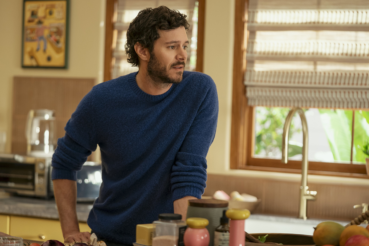 &Quot;A Man With Curly Hair And A Beard Wearing A Blue Sweater Stands In A Cozy Kitchen Leaning On The Counter, Surrounded By Cooking Ingredients, With Sunlight Coming Through The Window Blinds.&Quot;
