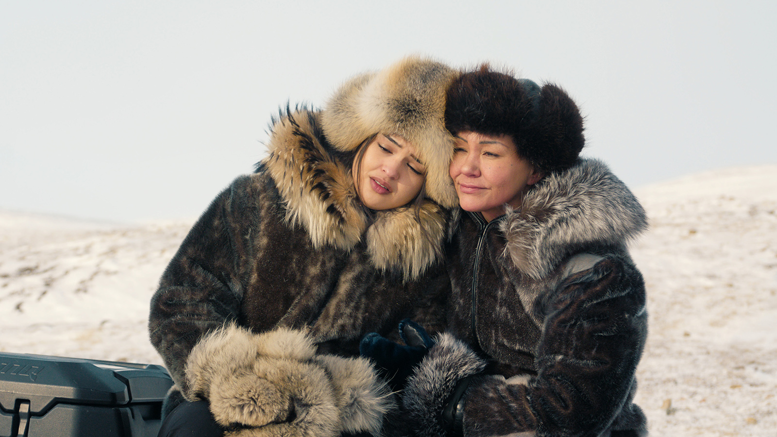 &Quot;Two People Wearing Thick Fur Coats And Hats Sit Close Together Outdoors, Surrounded By A Snowy Landscape, Sharing A Peaceful Moment In The Cold Environment.&Quot;