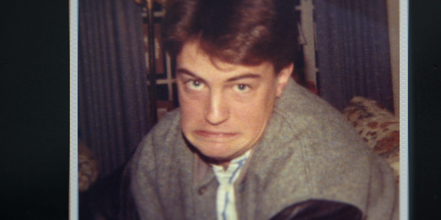 &Quot;Young Man With Brown Hair Making A Humorous, Exaggerated Facial Expression Indoors. He Is Wearing A Grey Jacket. The Background Features Curtains And Furniture, Suggesting A Casual Home Setting.&Quot;